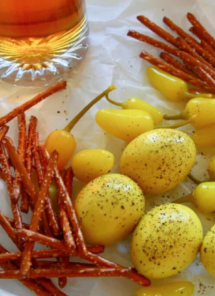 Crinkled parchment paper with a mug of beer, yellow pickled eggs, and pretzel sticks.