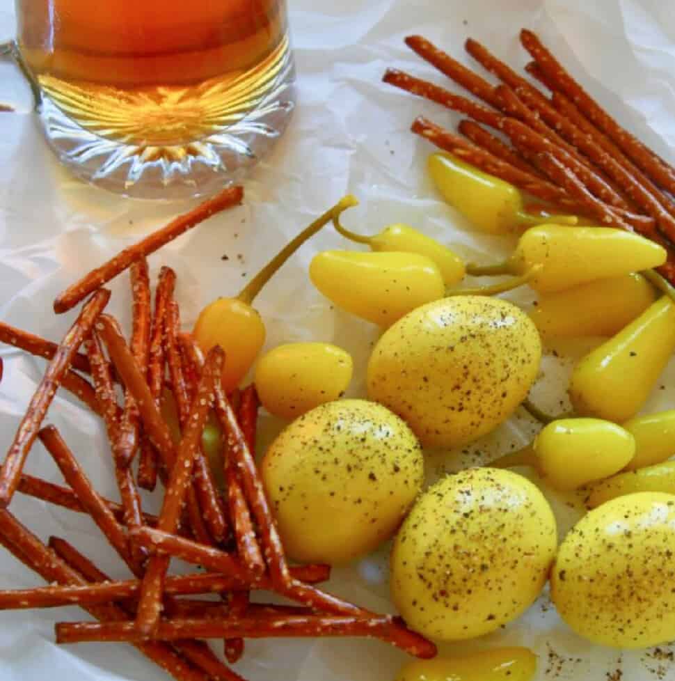 Crinkled parchment paper with a mug of beer, yellow pickled eggs, and pretzel sticks.