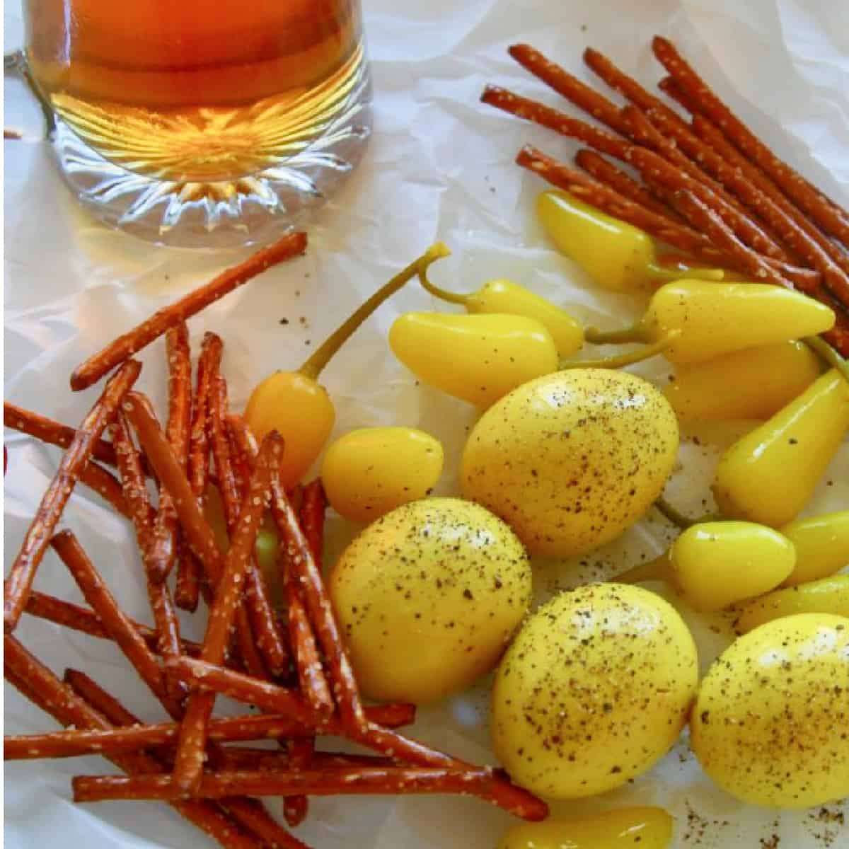 Crinkled parchment paper with a mug of beer, yellow pickled eggs, and pretzel sticks.