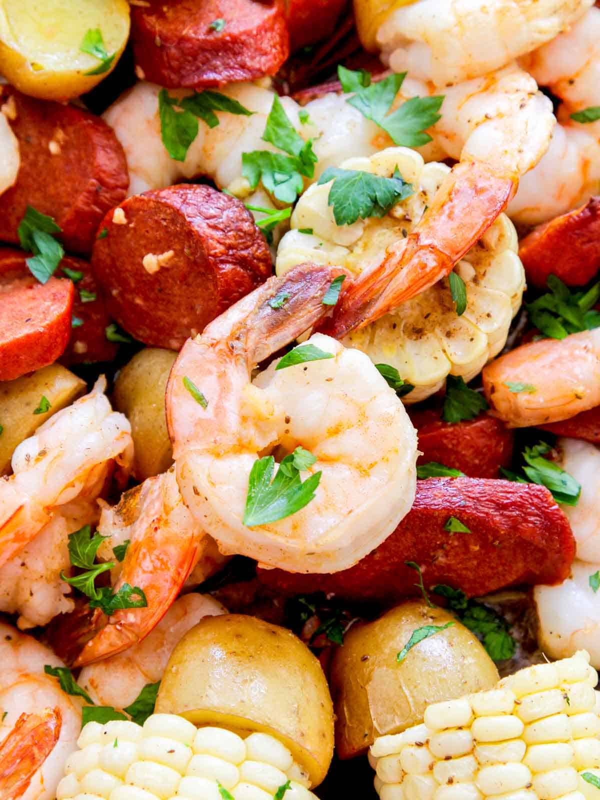 A close up of cooked shrimp, pieces of corn, sausage, and small potatoes on a sheet pan to bake for dinner. 