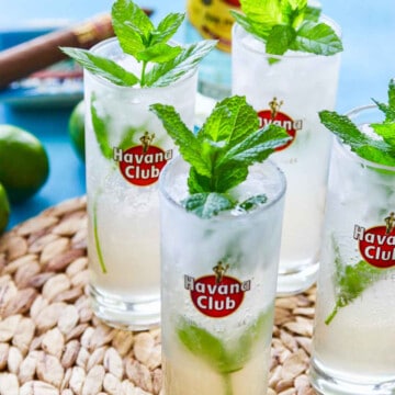 Four Havana club glasses filled with mojitos garnished with mint.