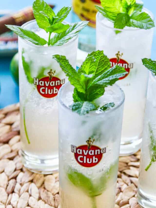 Four Havana club glasses filled with mojitos garnished with mint.