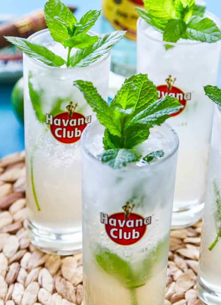 Four Havana club glasses filled with mojitos garnished with mint.