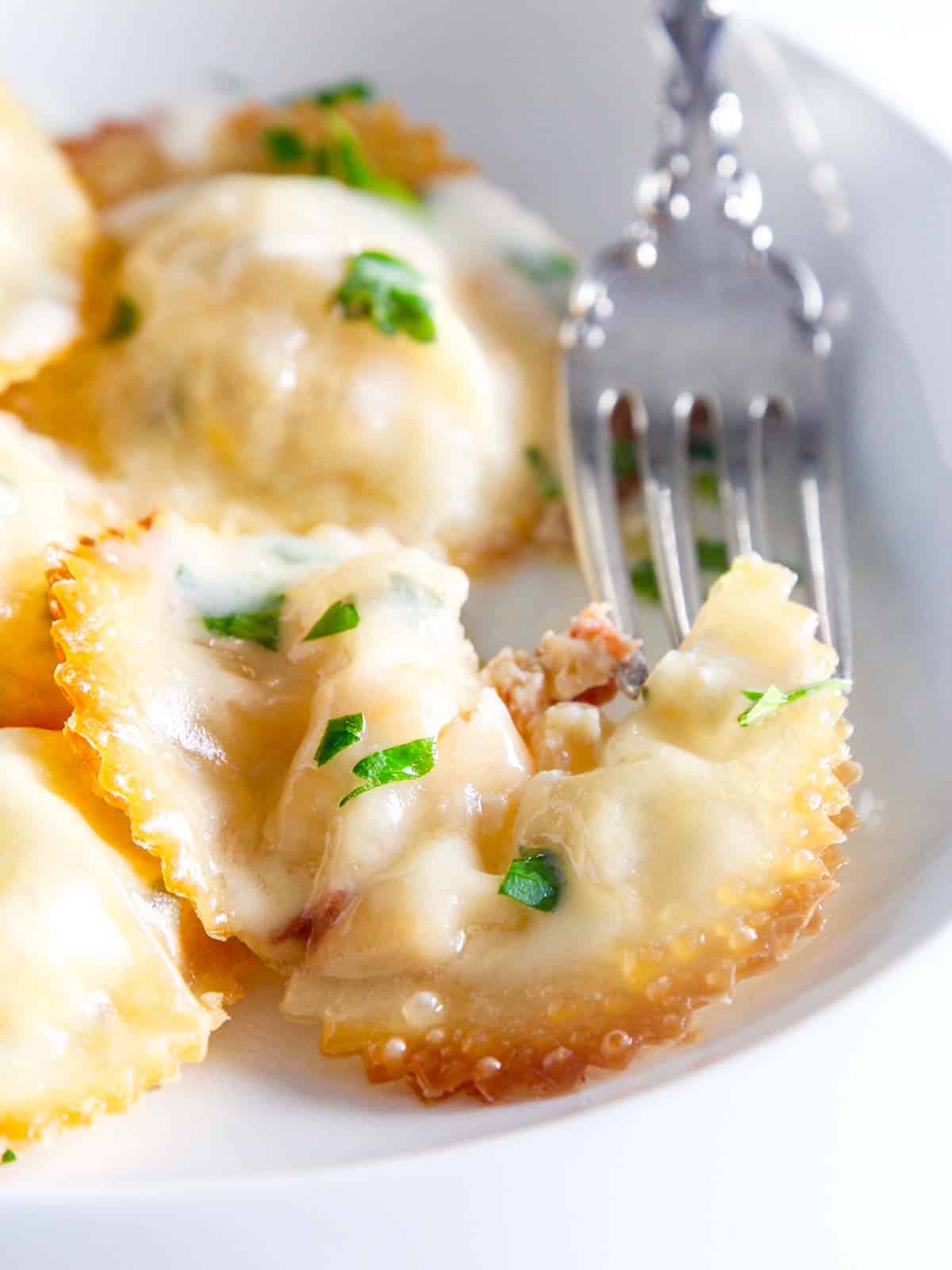 A silver fork cutting into a lobster ravioli on a white china plate. 