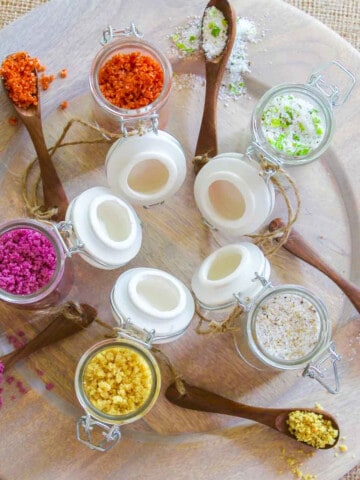 A wood platter with 5 seasoning jars open filled with flavored finishing salts.