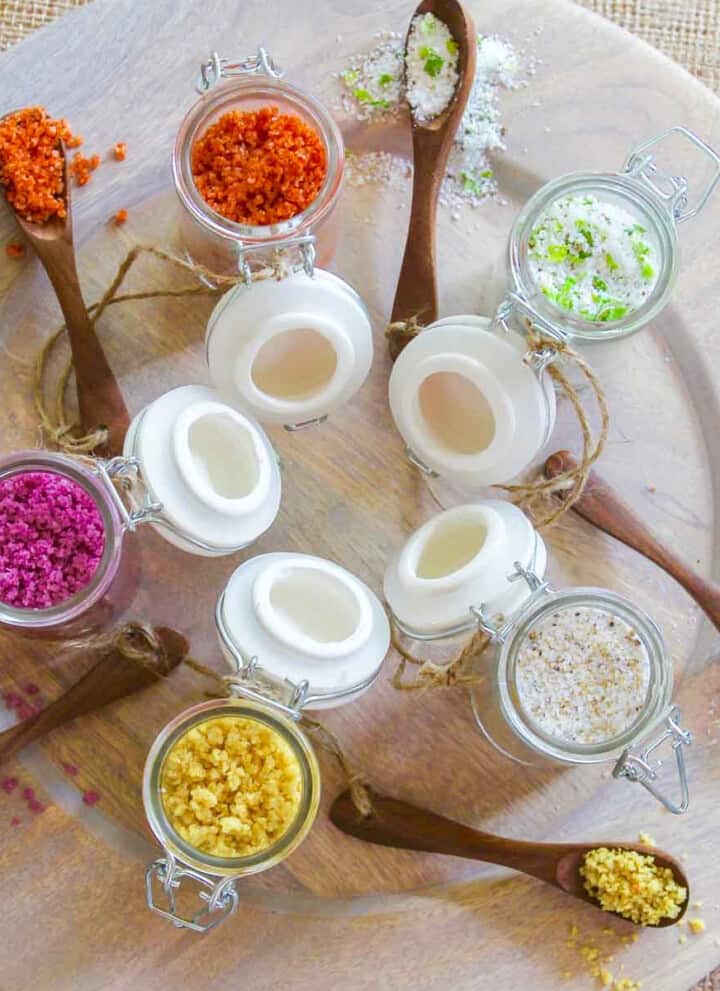 A wood platter with 5 seasoning jars open filled with flavored finishing salts.