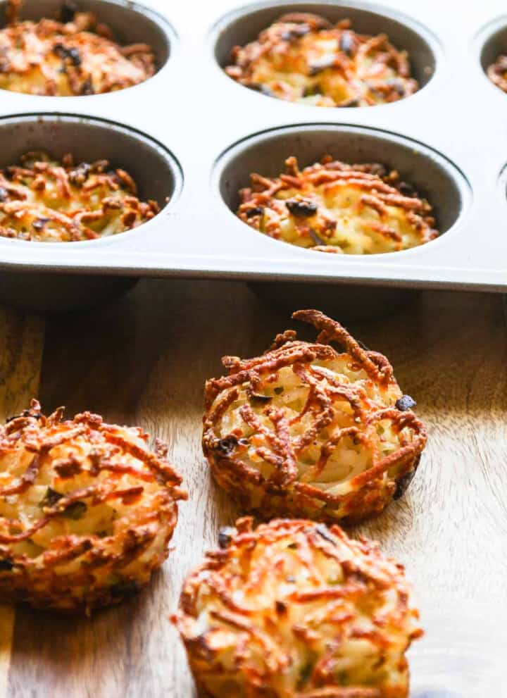 Three golden crispy edged hash browns baked in a muffin tin on cutting board.