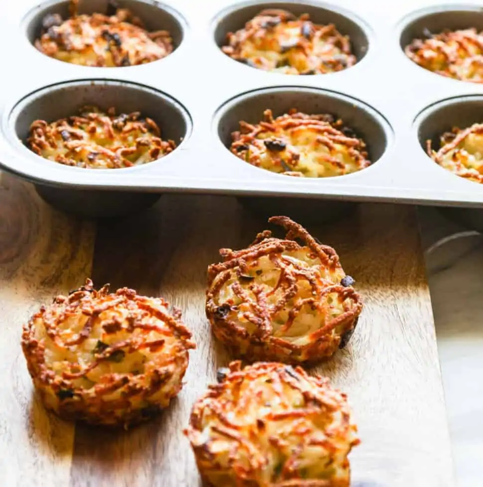 Three golden crispy edged hash browns baked in a muffin tin on cutting board.