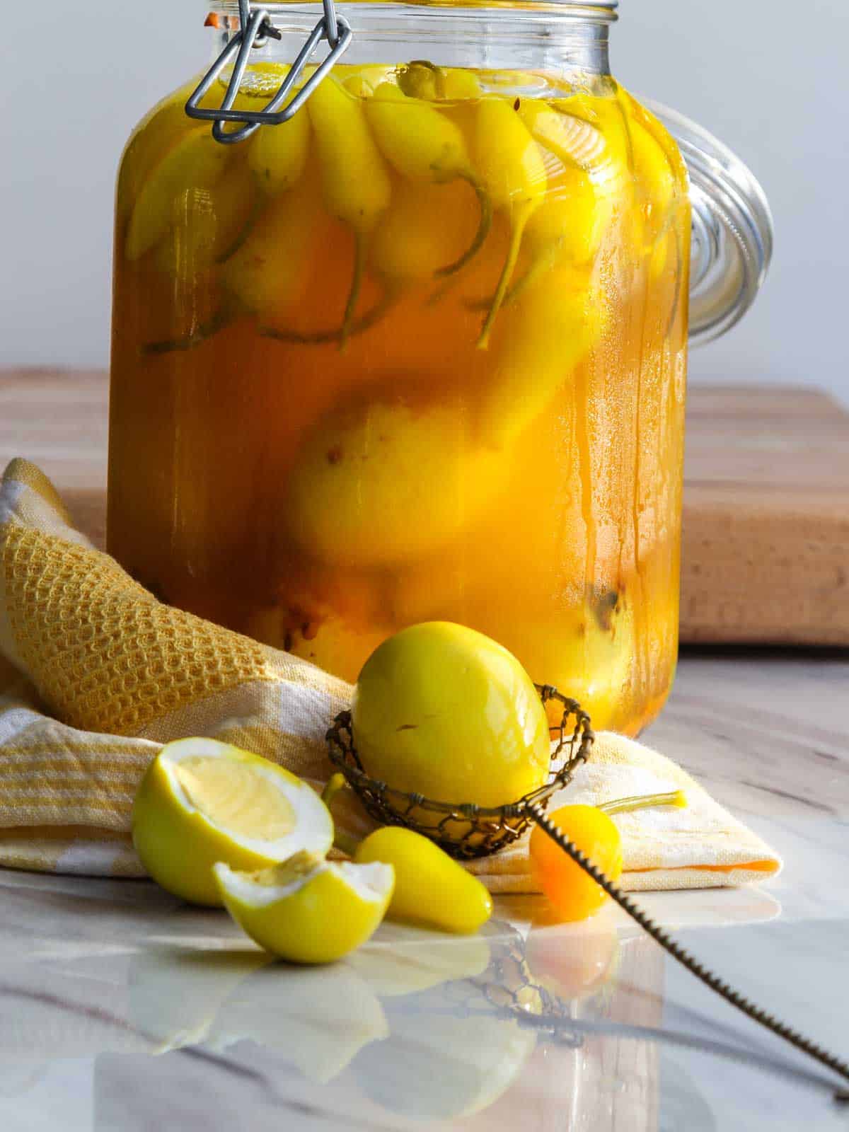 A large 2 quart jar filled with yellow pickled eggs, spices, and yellow chilis with one scooped out with a wire spoon on a towel.