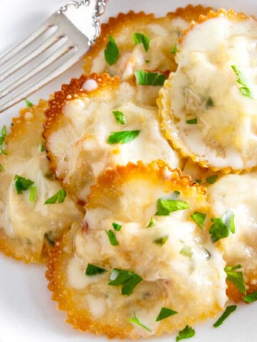 A white plate filled with heart shaped lobster ravioli garnished with parsley.