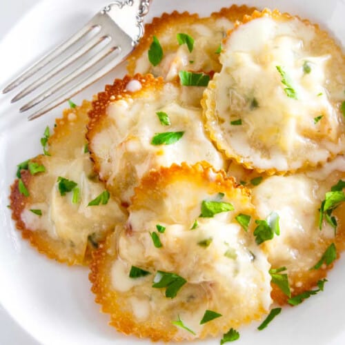 A white plate filled with heart shaped lobster ravioli garnished with parsley.