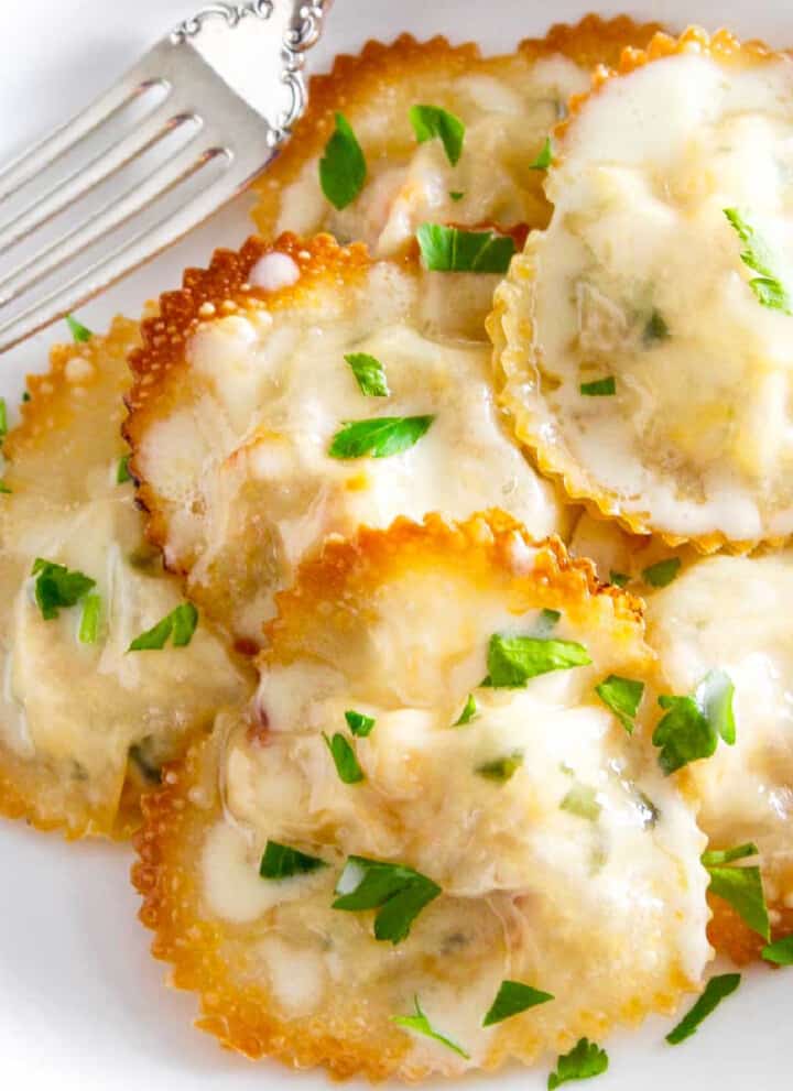 A white plate filled with heart shaped lobster ravioli garnished with parsley.