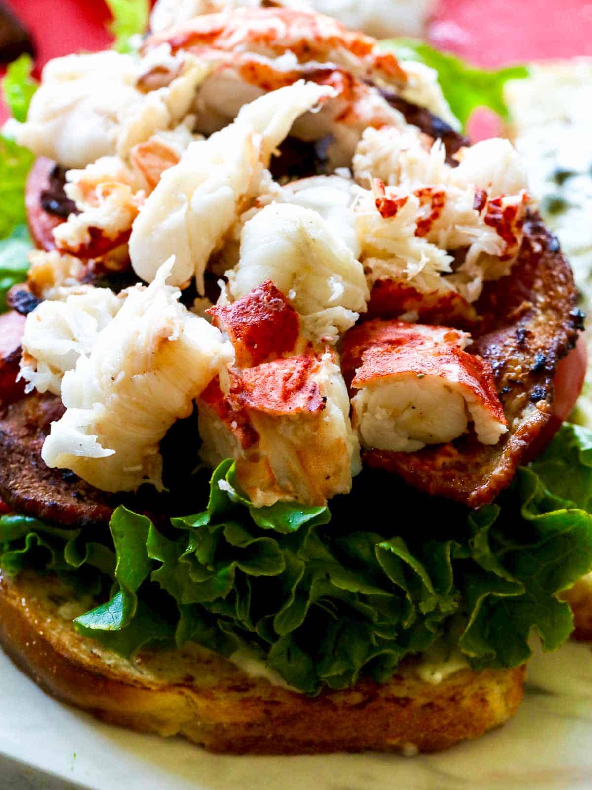 Assembly of a lobster BLT sandwich with bread, lettuce, tomato, bacon, and lobster meat.