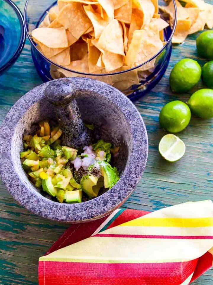 Looking down onto a table with molcajete holding ingredients for guacamole with chips and avocados.