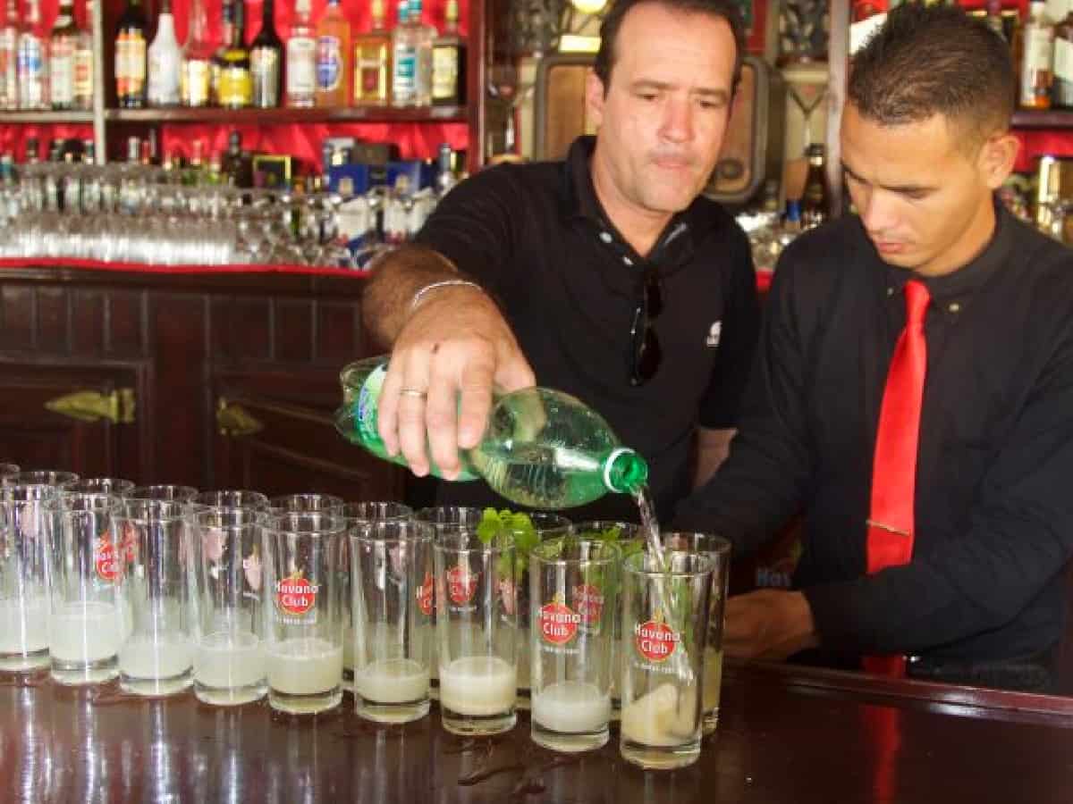 A bartender pouring lime juice into mojitos on a bar counter in glasses. 