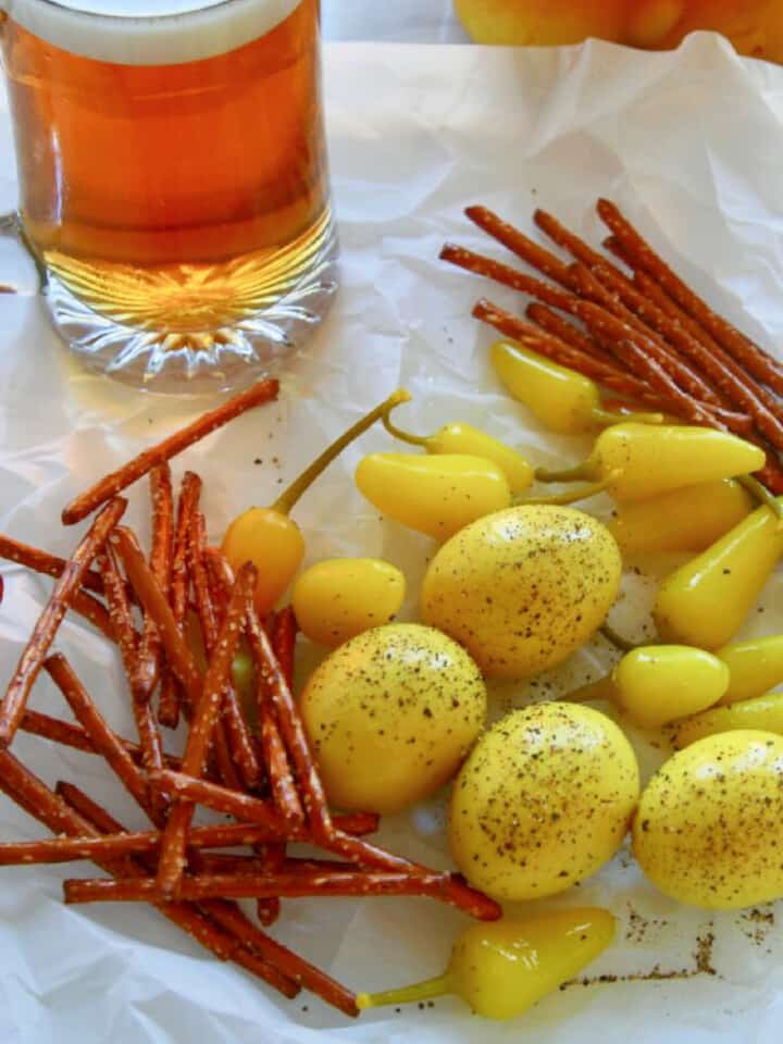 Crinkled parchment paper with a mug of beer, yellow pickled eggs, and pretzel sticks.