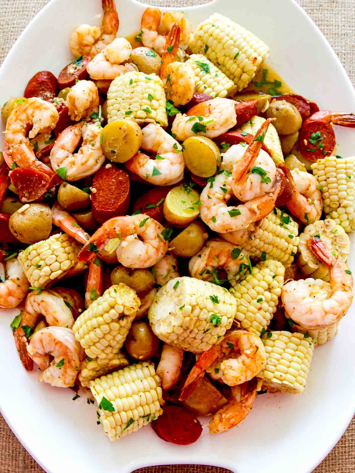 Looking overhead of a shrimp boil poured onto a platter including cooked shrimp, pieces of corn, sliced andouille sausage, and potatoes. 