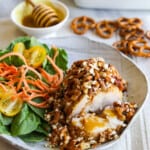 A piece of chicken coated in a pretzel crust and and salad on the plate for a honey mustard chicken recipe.