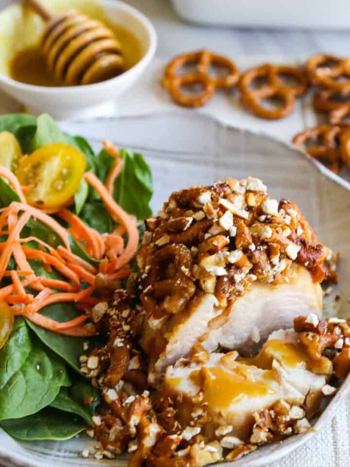 A piece of chicken coated in a pretzel crust and and salad on the plate for a honey mustard chicken recipe.