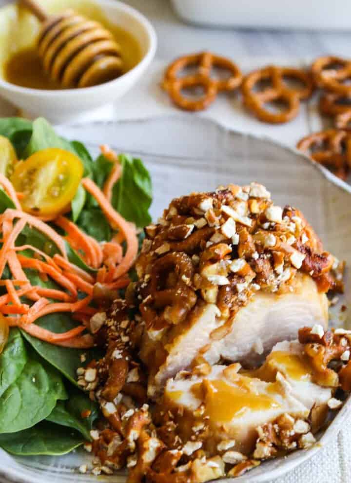A piece of chicken coated in a pretzel crust and and salad on the plate for a honey mustard chicken recipe.