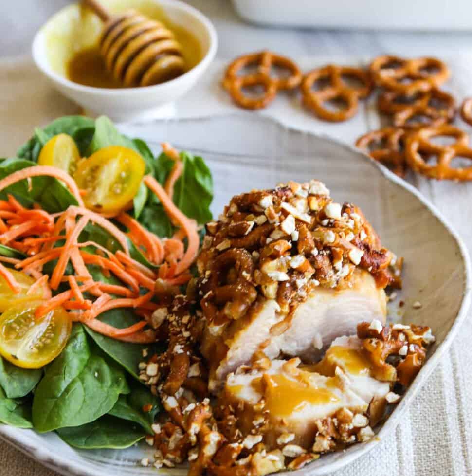 A piece of chicken coated in a pretzel crust and and salad on the plate for a honey mustard chicken recipe.