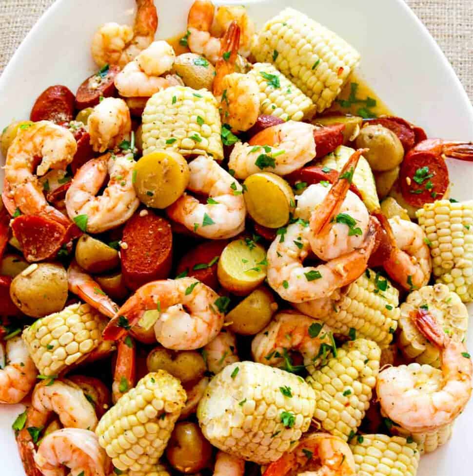 A white platter filled with corn, shrimp, sausage, and potatoes for dinner.