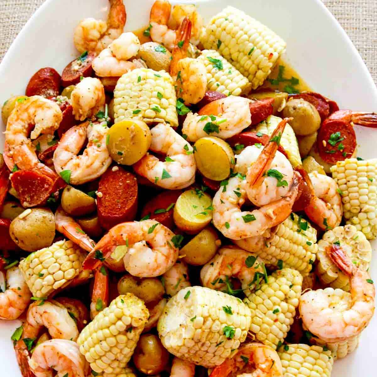 A white platter filled with corn, shrimp, sausage, and potatoes for dinner.