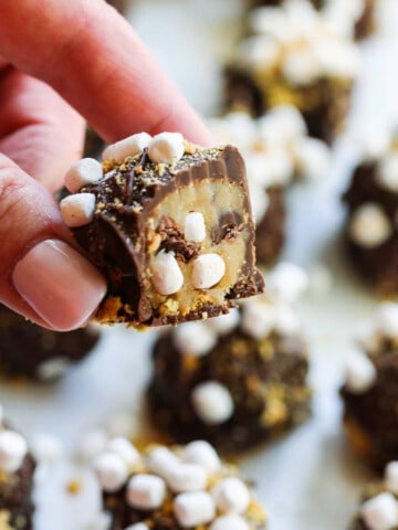 A lady holding a s'more cookie dough truffle cut open with mini marshmallows inside.