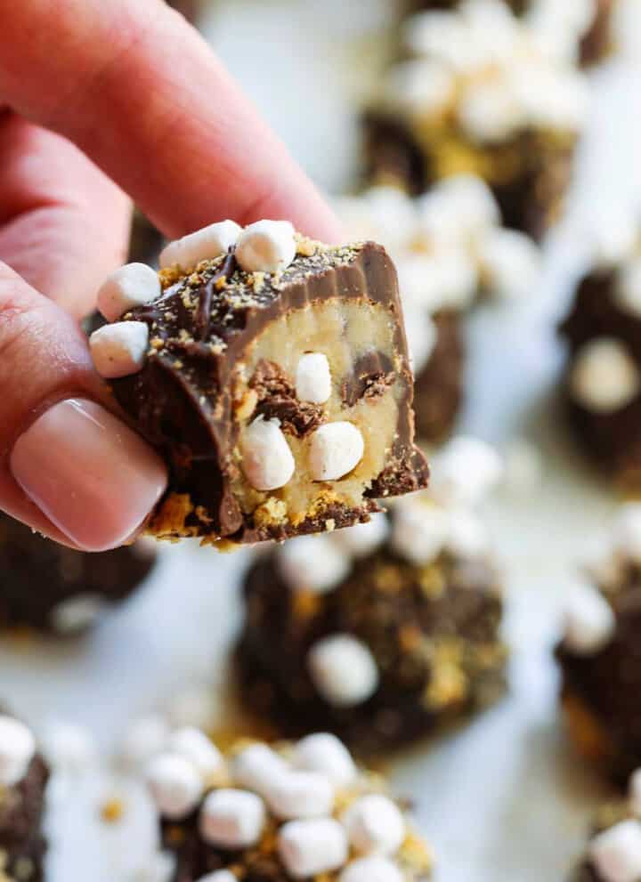 A lady holding a s'more cookie dough truffle cut open with mini marshmallows inside.