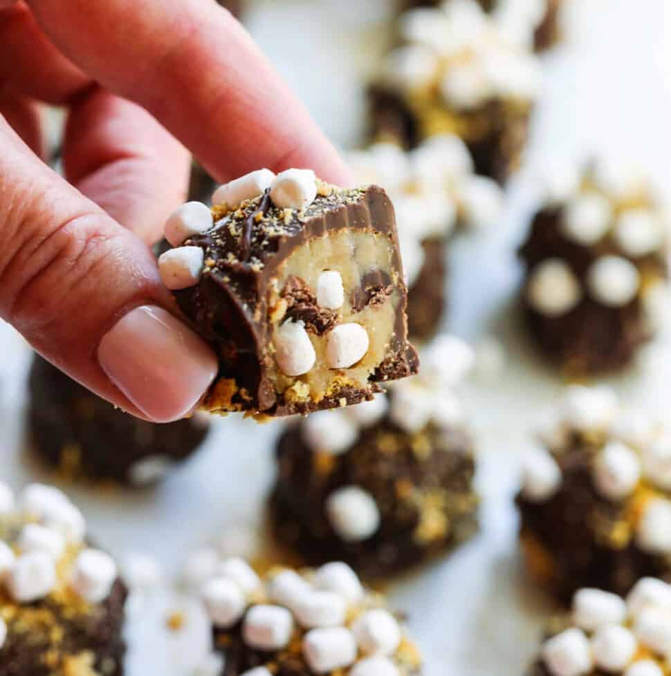 A lady holding a s'more cookie dough truffle cut open with mini marshmallows inside.