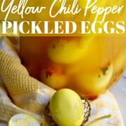 A large jar of pickled eggs and yellow peppers with one pulled out on a kitchen towel.