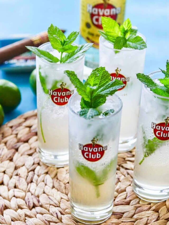 Four Havana club glasses filled with mojitos garnished with mint.