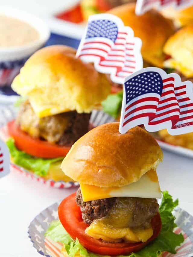 Small cheeseburger sliders with lettuce, tomato, and cheese with an American flag pick on top.