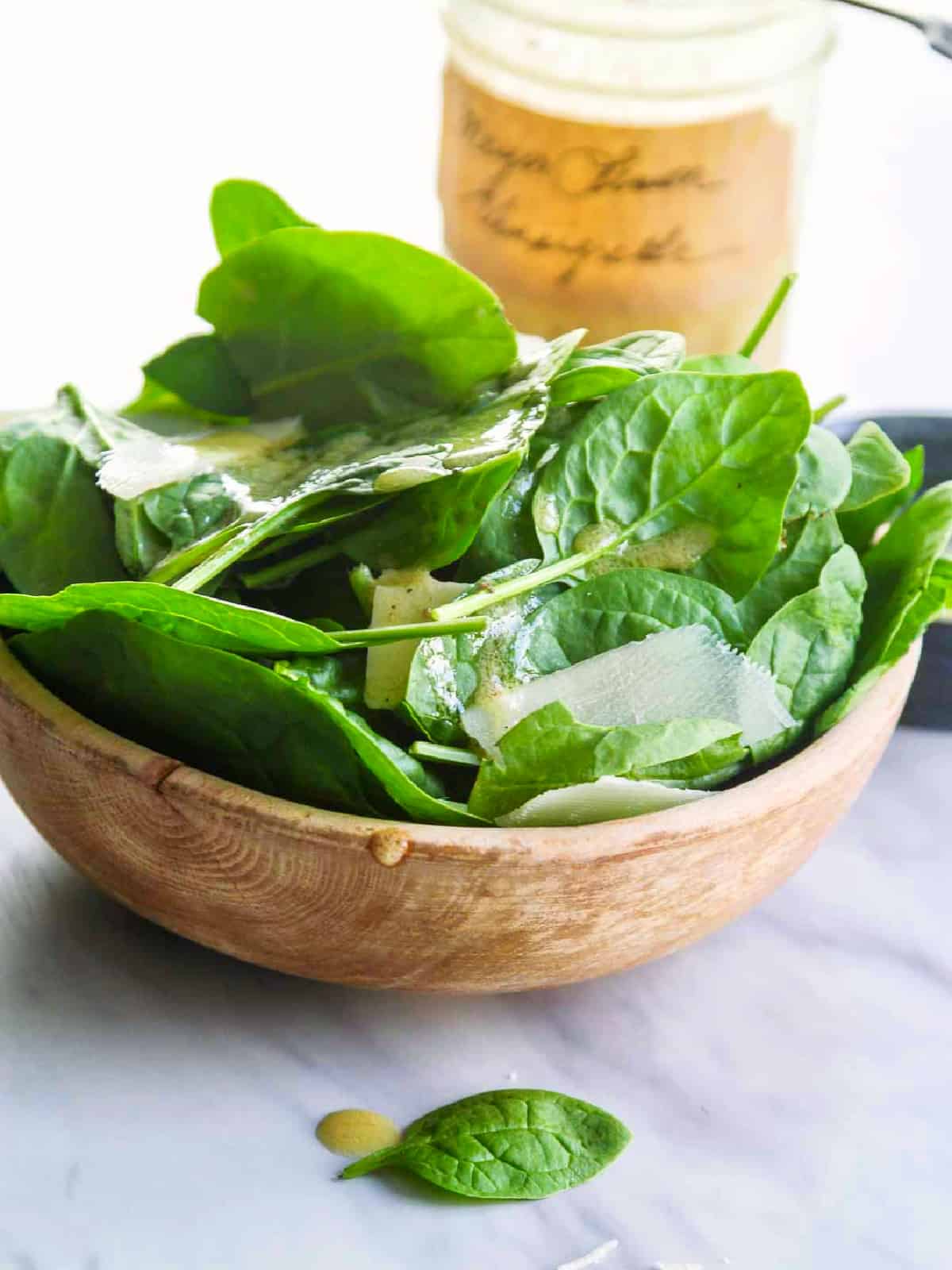 A small wooden bowl filled with fresh spinach, parmesan cheese shavings and vinaigrette.
