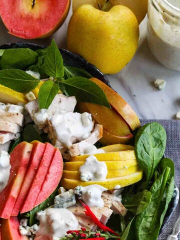 A ceramic plate with sliced apples, chicken on lettuce with homemade blue cheese dressing.