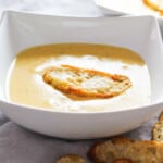 White bowl filled with cheese soup and a homemade crouton on top.