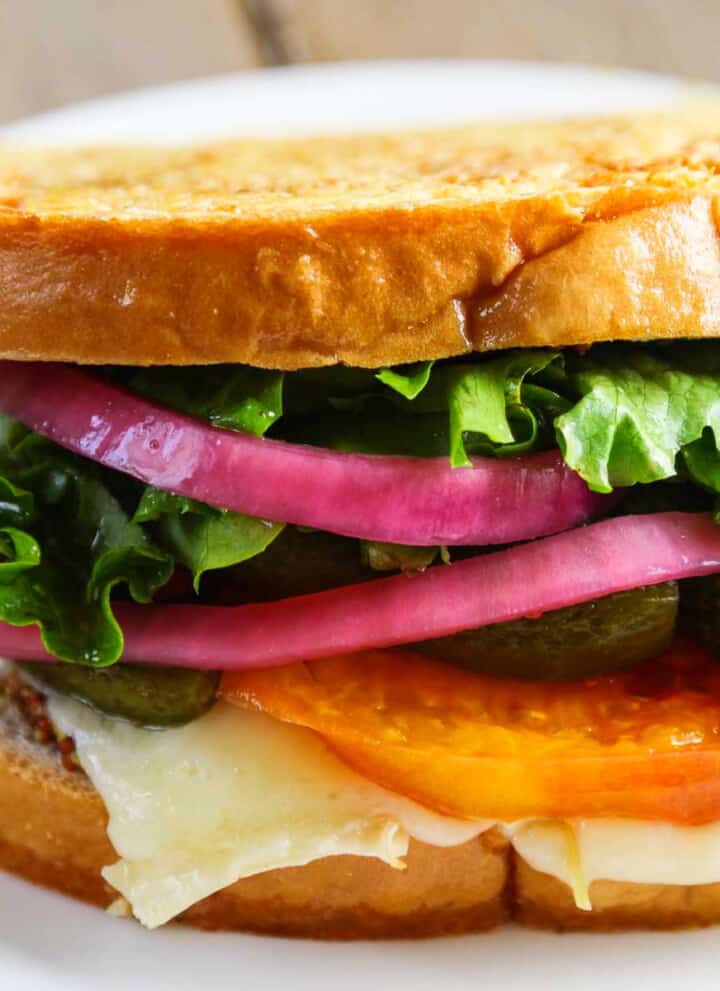 A stacked gourmet grilled cheese sandwich with cheese, tomato, red onions, and lettuce.