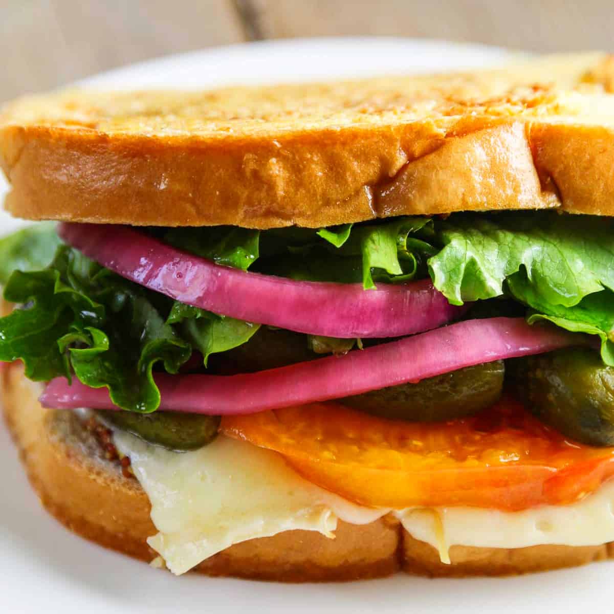 A stacked gourmet grilled cheese sandwich with cheese, tomato, red onions, and lettuce.