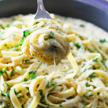 A fork holding twirled fettuccine out of a large skillet.