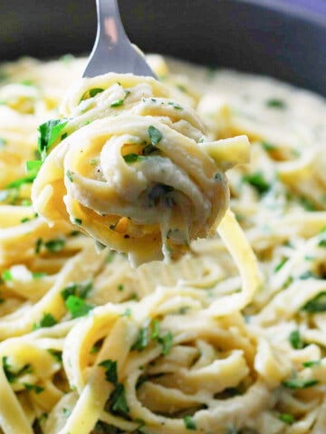 A fork holding twirled fettuccine out of a large skillet.