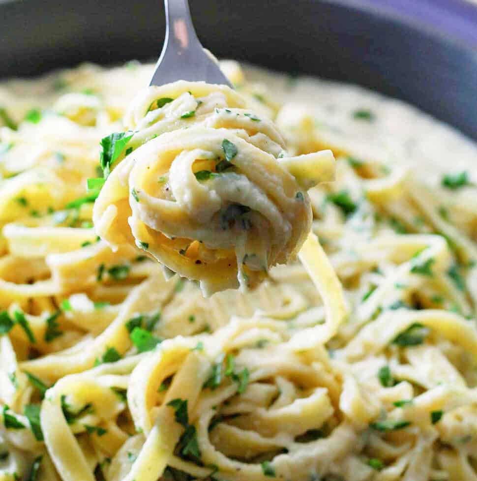 A fork holding twirled fettuccine out of a large skillet.