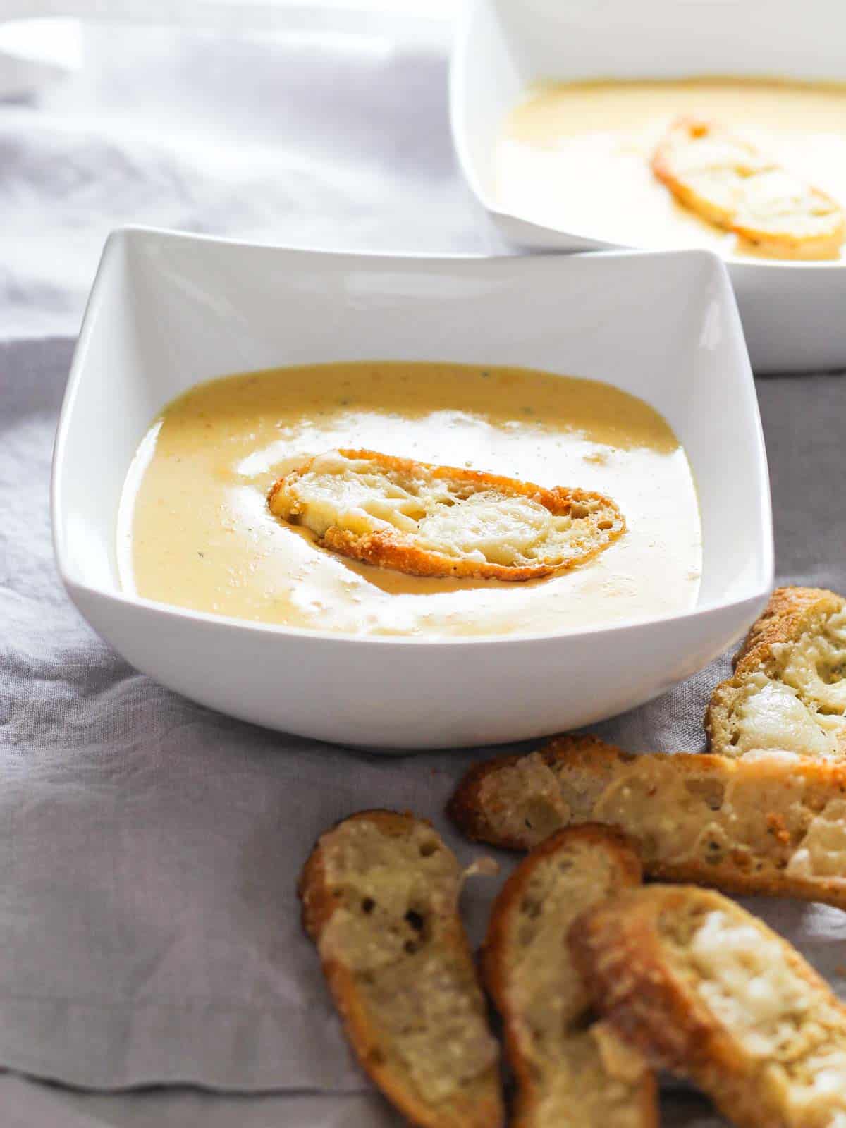 Square white bowl with cheese soup and a large crouton on top.