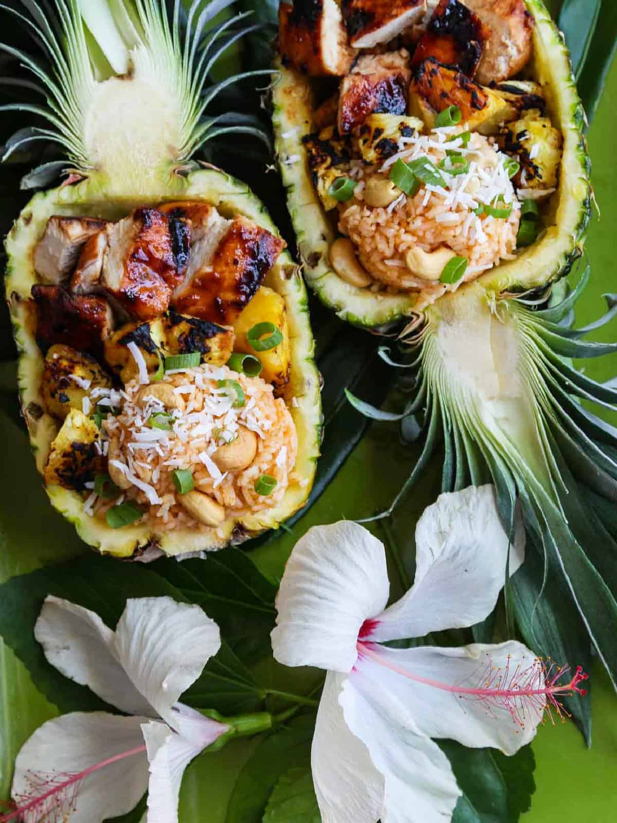 Two hibiscus flowers with pineapple halves filled with huli chicken, rice, and pineapple.