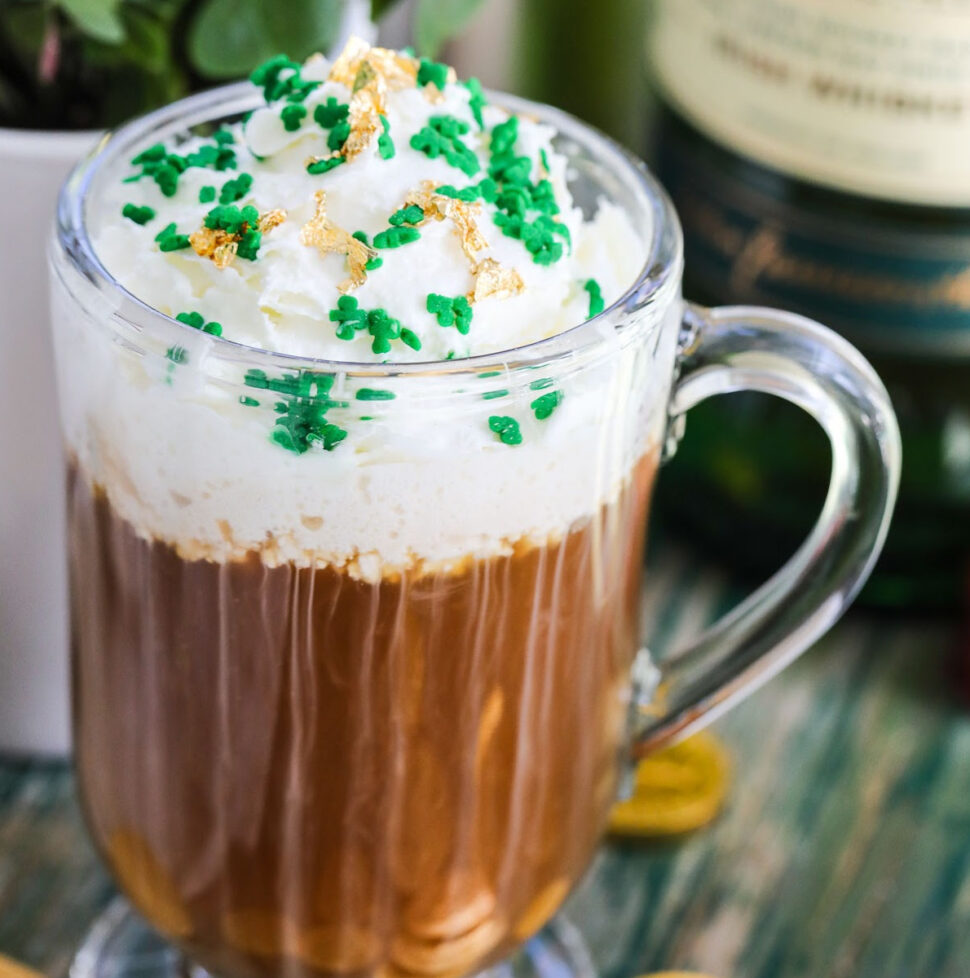 A glass mug with Irish Coffee on a vintage green table topped with green sprinkles and edible gold.