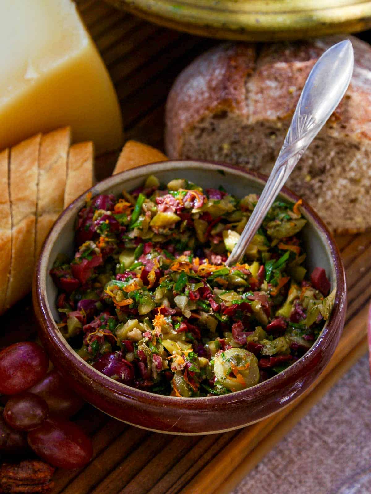 A vintage bowl with green olive tapenade and bread nearby.
