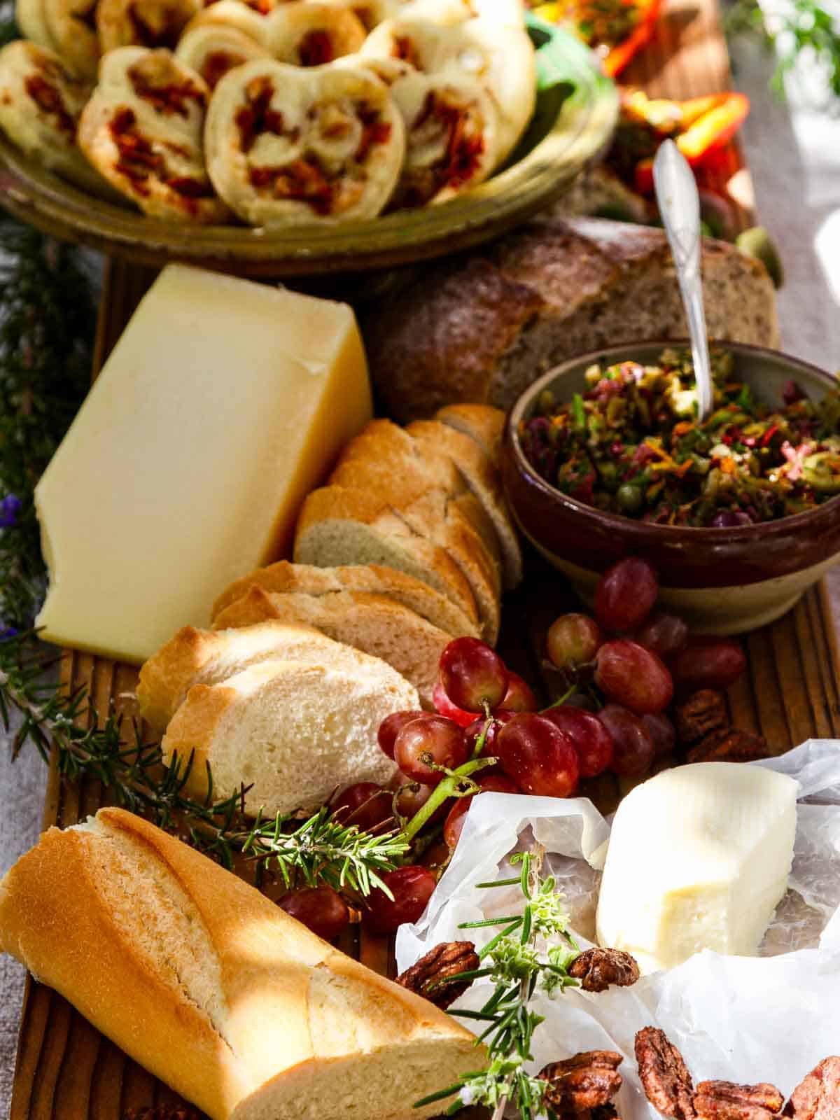 An outdoor picnic with cheeses, sliced loaf of French bread, grapes, and olive tapenade.