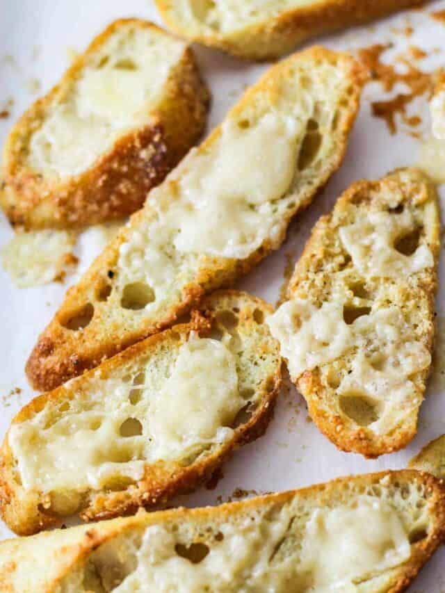 Baguette crouton shards with melted cheese on a parchment paper lined baking tray.