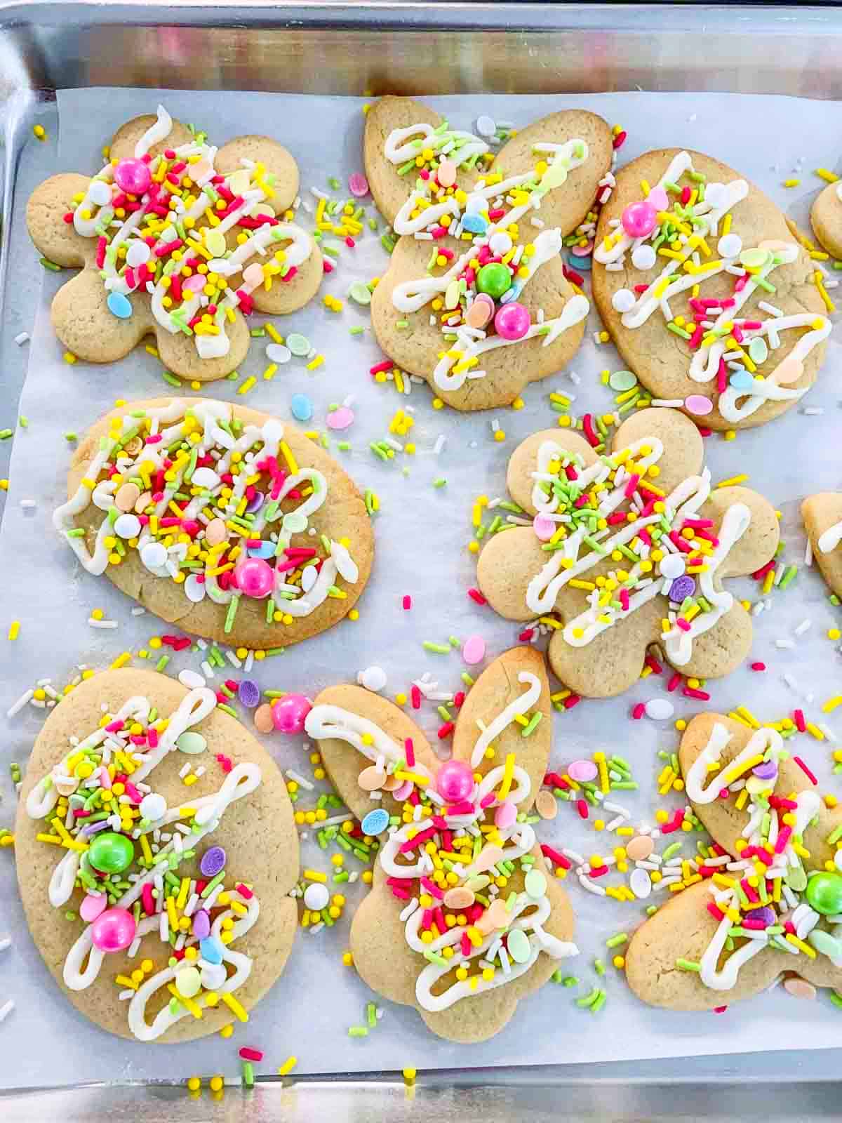 A large sheet pan lined with parchment paper and baked and decorated Easter cookies with sprinkles and icing.