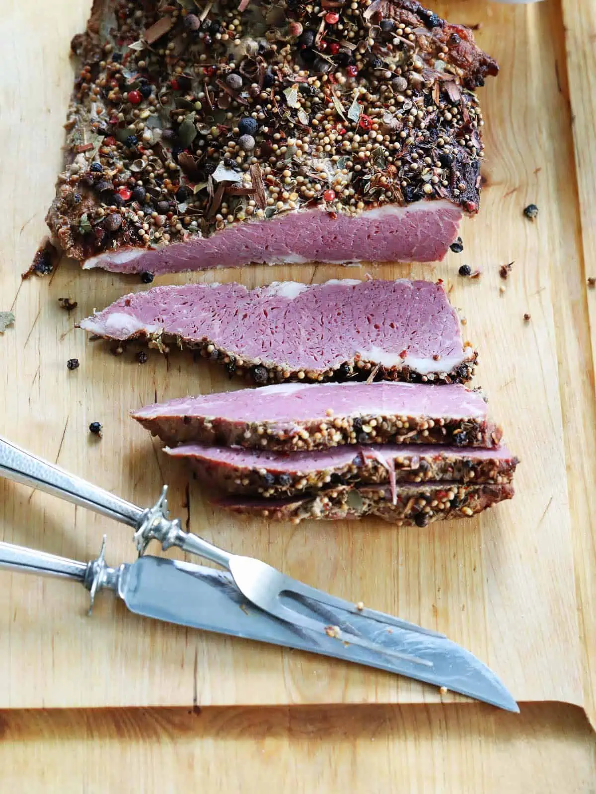 Long slices of corned beef brisket on a wood cutting board with a silver carving set.
