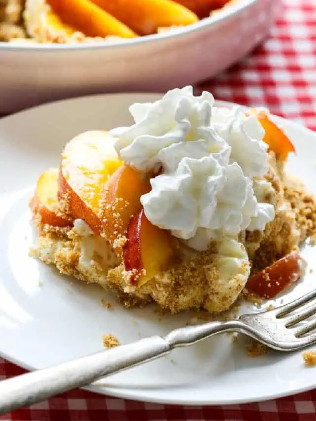 A slice of peach pie on a white plate with a silver fork on a red white check tablecloth.